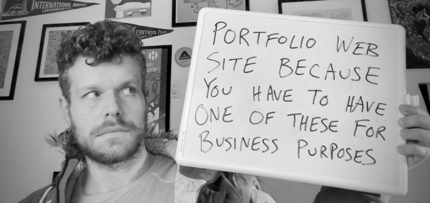 A scruffy man in his late 30s holding a white board reading 